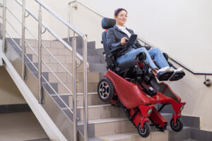 A woman using an electric wheelchair equipped with stair-climbing technology, safely descending a flight of stairs with the assistance of her specialized wheelchair.